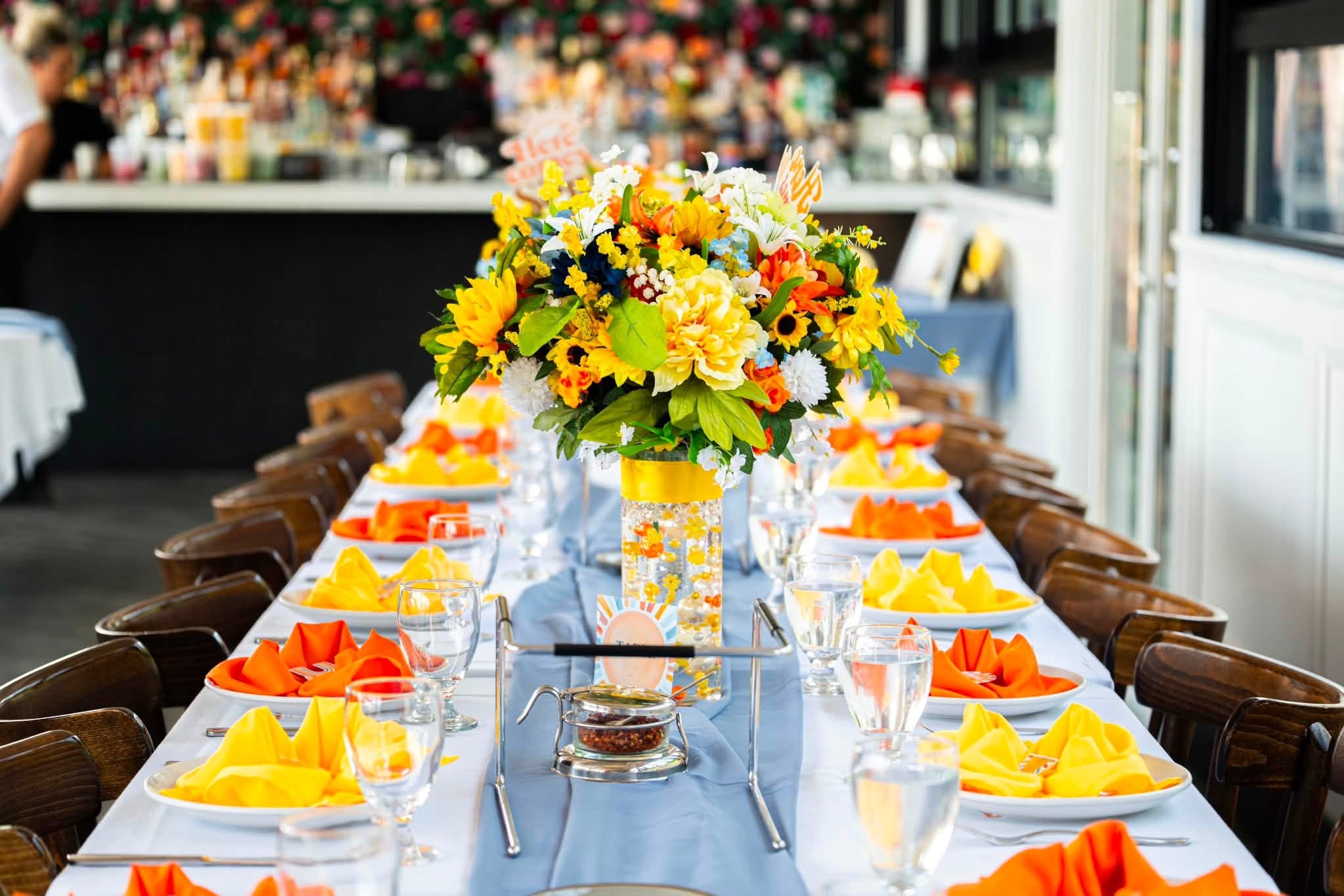 Close-up of a Rooftop tablescape with sunflower centerpiece, folded napkins and the bar beyond